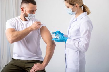 Doktor, erkek hastaya koronavirüs aşısı yapmadan önce elinde şırınga tutuyor..