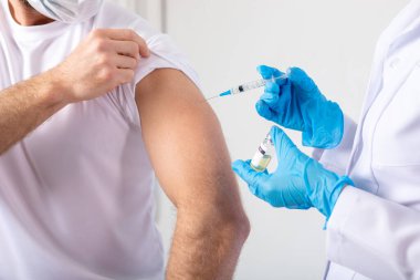 Doktor, erkek hastaya koronavirüs aşısı yapmadan önce elinde şırınga tutuyor..