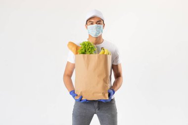 A delivery man in a protective mask and gloves holds a craft bag with groceries.