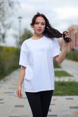 Kendine güvenen genç bir kadın şık, büyük boy beyaz bir tişörtle poz veriyor. Zarif bir şekilde şık taytlarla eşleştirilmiş.