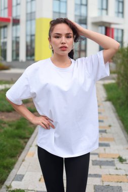 Tarz sahibi genç bir kadın, modaya uygun beyaz bir bluz ve siyah tozluklarla modern bir arkaplanda rahatça poz veriyor..