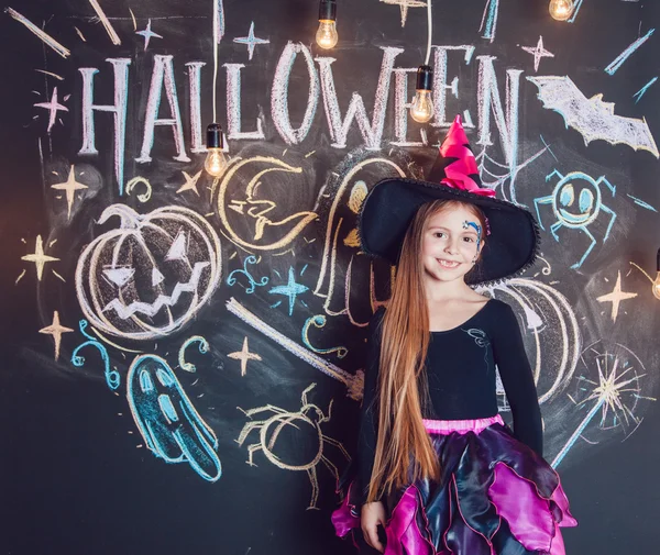 Menina vestida com trajes de Halloween. Posando no fundo da inscrição Halloween . — Fotografia de Stock