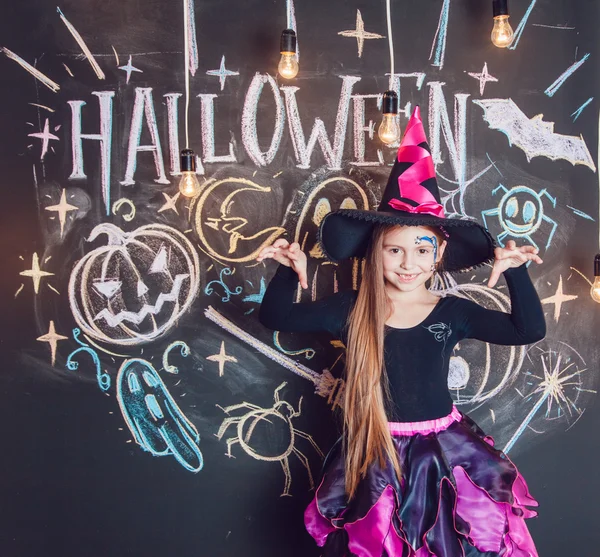 女の子のハロウィーンの衣装を着てください。ハロウィーンの銘刻文字の背景にポーズ. — ストック写真