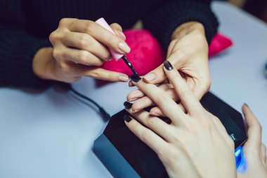 Manikür. Güzellik Salonu. Yakın çekim. Siyah oje uygulamak.