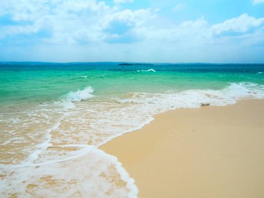 Turkuaz okyanus dalgalarının kumsaldan manzarası ve bulutlu mavi gökyüzü. Zanzibar, Tanzanya.