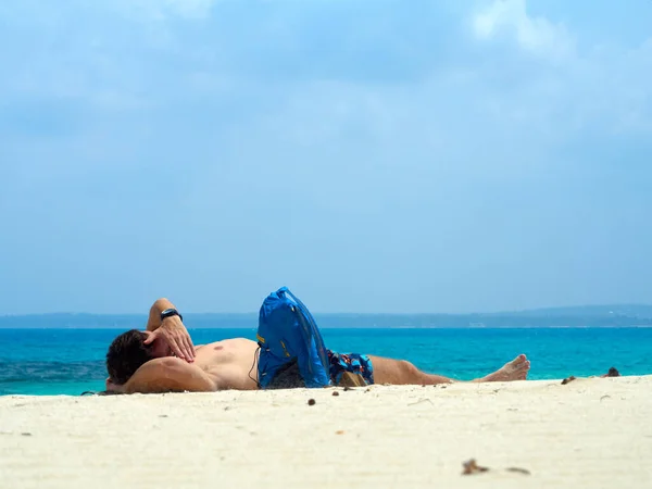 Sahilde güneş banyosu yapan bir adam, arkasında kumsal ve mavi gökyüzü olan bir adam. Hapishane Adası. 