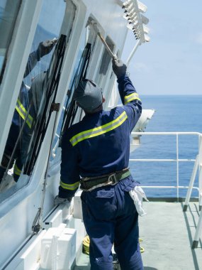 Güverte çalışanı, mavi tulumlu sıradan bir denizci köprüyü beyaz renge boyuyor..