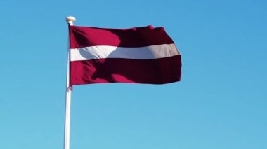 Letonya 'nın ulusal bayrağı bayrak direğinde rüzgarda sallanıyor..