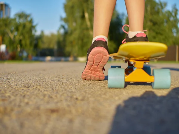 Menina garoto de pé na estrada de asfalto e placa de centavo amarelo com rodas azuis no fundo da rua durante o pôr do sol. Fotografia De Stock