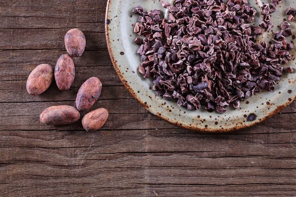 Raw Cacao Nibs and cacao beans over rustic wooden background