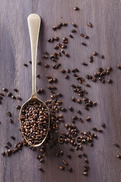 Grani di orzo nero su cucchiaio di metallo su fondo di legno rustico — Foto Stock