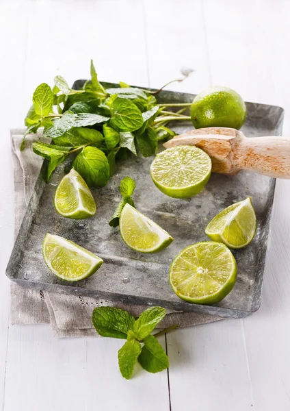 Limes quarters and mint leaves over white wooden background — Stock Photo, Image