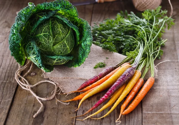 Savoy cabbage and colored carrots over rustic wooden background — Stock Photo, Image