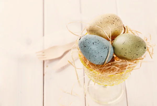 Pastel colored Easter eggs in straw basket — Stock Photo, Image