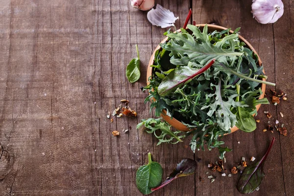 Leafy green mix over rustic wooden background with copy cpase