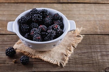 Ahşap rustik arka plan üzerinde beyaz kevgir içinde böğürtlen