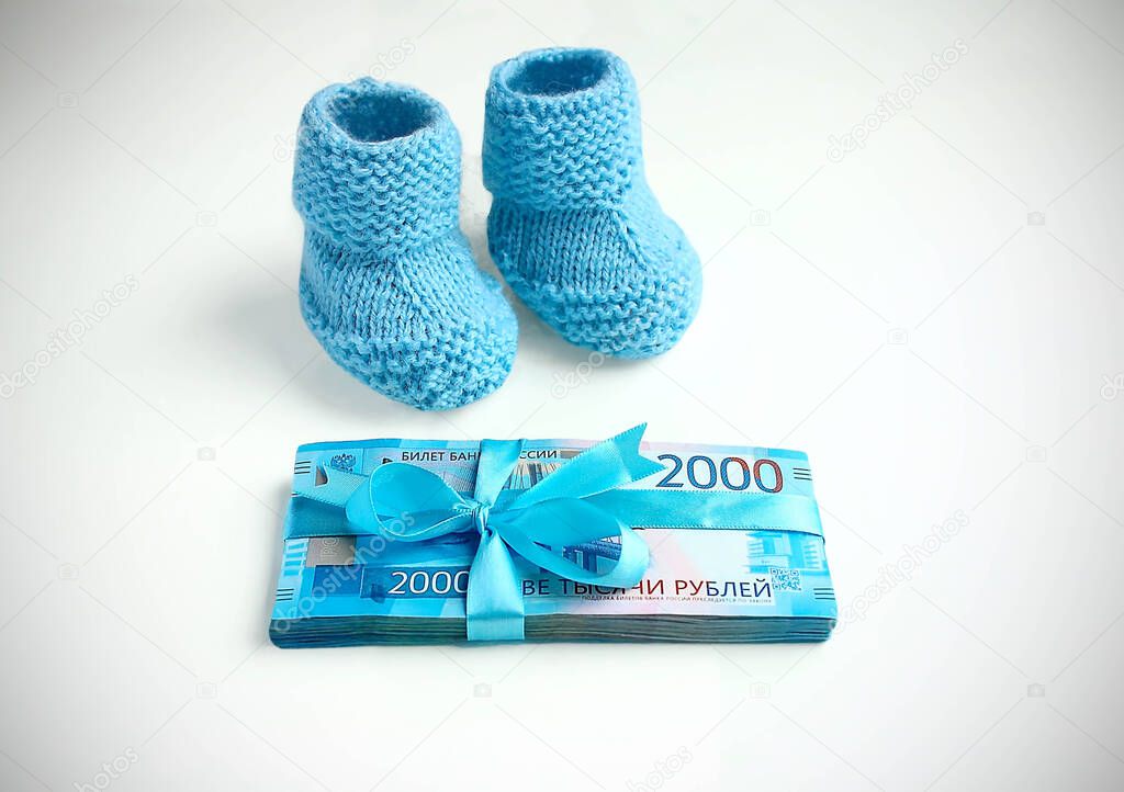 Maternal capital, childbirth. Blue knitted baby booties and two thousand rubles with a blue ribbon bow.