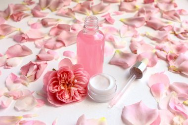 Cilt bakım kozmetiği. Gül suyu ve gül yapraklarının arka planında yüz kremi.