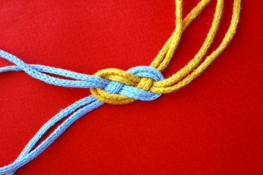 Kırmızı zemin üzerinde mavi ve sarı renkli iki ipten yapılmış sekiz düğüm..