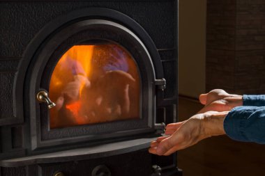 Evdeki şöminede elleri ısıtan bir adam. Ilık şöminede dinleniyor..