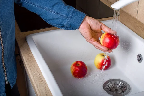 Man washes apples under the tap, close up.