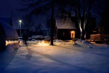 Bahçe karla kaplıydı, kış gecesi. Açık hava ışıkları yanıyor..
