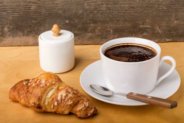 Kahveli beyaz fincan, kruvasan ve ahşap bir masada hamur işi. Kahvaltı konsepti.