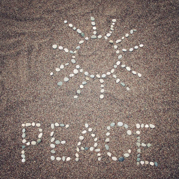 Слово мира и символ солнца на песке - тонированное фото . — стоковое фото