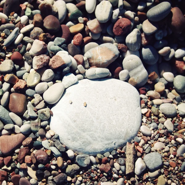 Stor rund vit sten bland grå och bruna stenar på stranden — Stockfoto