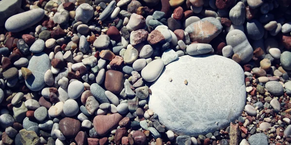 Большой круглый белый камень среди серой и коричневой гальки — стоковое фото