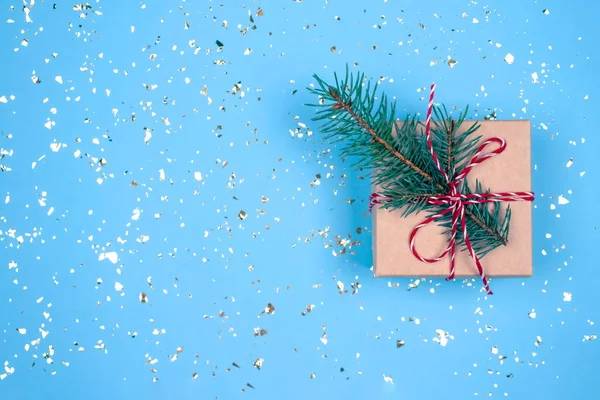 Caixa de presente com arco vermelho e galho de árvore de Natal no fundo azul festivo com brilhos dourados ao redor e espaço para o seu texto. Estilo leigo plano. Conceito de celebração de Natal ou Ano Novo — Fotografia de Stock