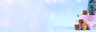 Noel ağacı, hediye kutuları, dekorasyonlar ve pastel mavisi arka plandaki bulanık bokeh ile modayla yeni yıl ve modaya uygun kompozisyona sahip pankart. Seçici odak
