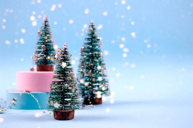 Trendy Christmas and New Year composition with Christmas trees, decorations and bokeh lights on pastel blue background with copyspace. Selective focus, place for text clipart