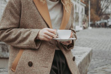 Central City caddesinde sabah kahvesi içen genç bir kadının yüzsüz görüntüsü. Sonbahar açık hava moda ayrıntıları, moda sokak kıyafeti giyen bir kadın. Şehirde gezgin blogcu