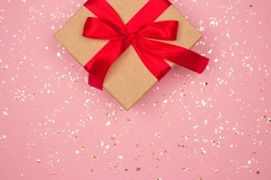 İçinde kırmızı fiyonk, pembe arka planda altın parıltılar ve metin için kopyalama alanı olan hediye kutusu. Düz yatış stili. Noel, Yeni Yıl, Sevgililer Günü ya da doğum günü kutlaması konsepti