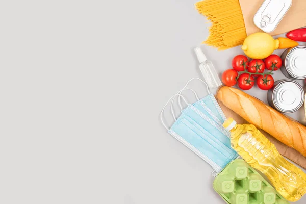 Flat lay composition with food and medicines donations on grey background with copyspace - pasta, fresh vegatables, canned food, baguette, cooking oil. Food donations or food bank concept