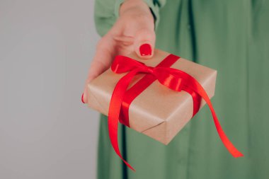 Elinde kırmızı kurdeleyle süslenmiş Noel hediyesi kutusu tutan genç bir kadın. Noel tatili ve yeni yıl kutlaması konsepti. Noel için aile hediyeleri hazırlıyorum.