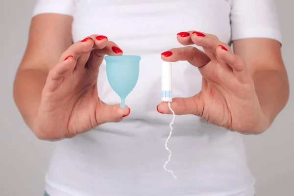 Mükemmel manikürlü kadın eli, elinde farklı tipte kadın hijyen ürünleri var - mavi regl kupası ve tampon. Kadın sağlığı ve hijyen kavramı, alternatif hijyen ürünleri — Stok fotoğraf