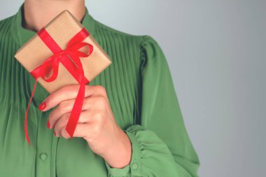 Yeşil elbise giyen, elinde kırmızı bant yayıyla süslenmiş Noel hediyesi kutusuyla yüzü olmayan genç bir kadının fotoğrafı. Noel tatili, yeni yıl ya da doğum günü kutlaması konsepti. Noel sezonu satışları