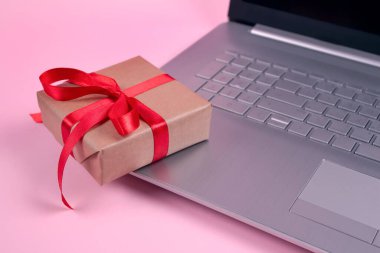Dizüstü bilgisayarda ön görüş ve metin için kopyalama alanı olan pastel pembe arka planda kırmızı fiyonklu mevcut kutu. Mevsimlik satış, Kara Cuma, online alışveriş ve siber pazartesi konsepti.
