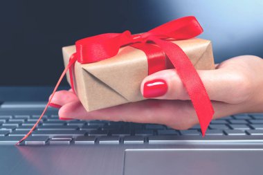 Projeniz için arka planda kırmızı yay ve dizüstü bilgisayarlı hediye kutusu olan bir kadın eli. Mevsimlik Noel indirimi, Kara Cuma, online alışveriş ve siber pazartesi konsepti.