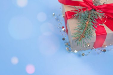Kırmızı fiyonklu hediye kutusu ve şenlikli mavi arka planda Noel ağacı dalı. Etrafında bokeh ışıkları ve metnin için kopyalama alanı var. Düz yatış stili. Noel veya Yeni Yıl Kutlama Konsepti