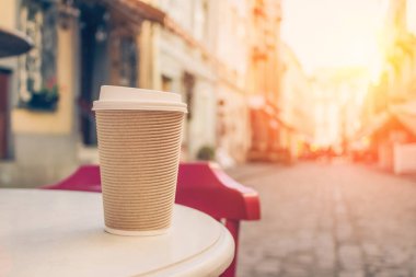 Arkadaki bulanık kafenin arka planında fotokopi alanı olan ahşap masanın üzerinde duran bir kahve fincanı görüntüsü. Geri dönüşümlü kağıt bardağa koymak için kahve.