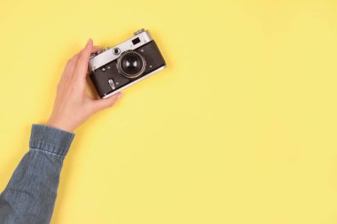 Gri ve sarı renkte kompozisyon, 2021 yılının rengi. Kadın eli, sarı arka planda, fotokopi alanı olan eski bir fotoğraf makinesini tutuyor. Çevrimiçi fotoğrafçılık okulu konsepti, seçici odak