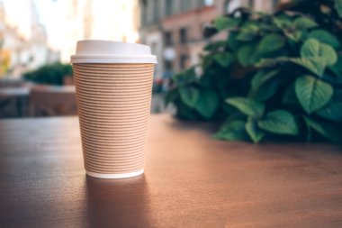 Geri dönüşümlü kağıt bardağa koymak için kahve. Kağıttan kahve fincanı görüntüsü, ahşap bir masanın üzerinde duruyor ve arkada bulanık bir kafe var, arka planda da da fotokopi var.