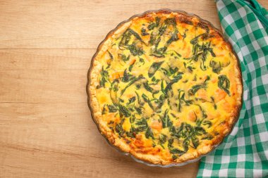 Top view on salmon fish and baby spinach leaves quiche pie - homemade recipe pie on wooden table background with copy space. Selective focus clipart