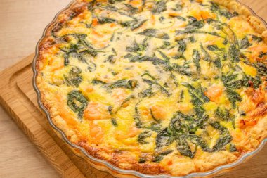 Deniz ürünleri ve somon balıklı kiş ve bebek ıspanaklı turta. Ahşap masa arkasında ev yapımı tart. Fotokopi alanı seçici bir odak noktası var.