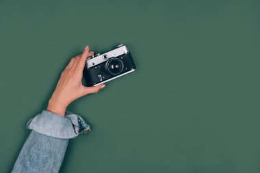 Yeşil zemin üzerinde eski bir retro fotoğraf makinesini tutan kadın. Metin için fotokopi alanı var. Eski moda fotoğrafçılık, online fotoğrafçılık okulu konsepti. Seçici odak