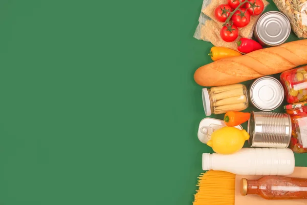 Different groceries or food donations on green background with copy space - pasta, fresh vegatables, canned food. Food bank or food delivery concept, Christmas or Easter donations