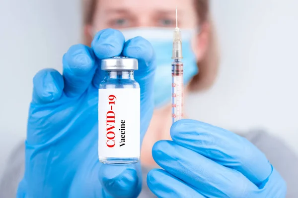 Female doctor or woman scientist wearing medical face mask and holding COVID-19 vaccine - protection against coronavirus, global vaccination concept. Selective focus — Stock Photo, Image